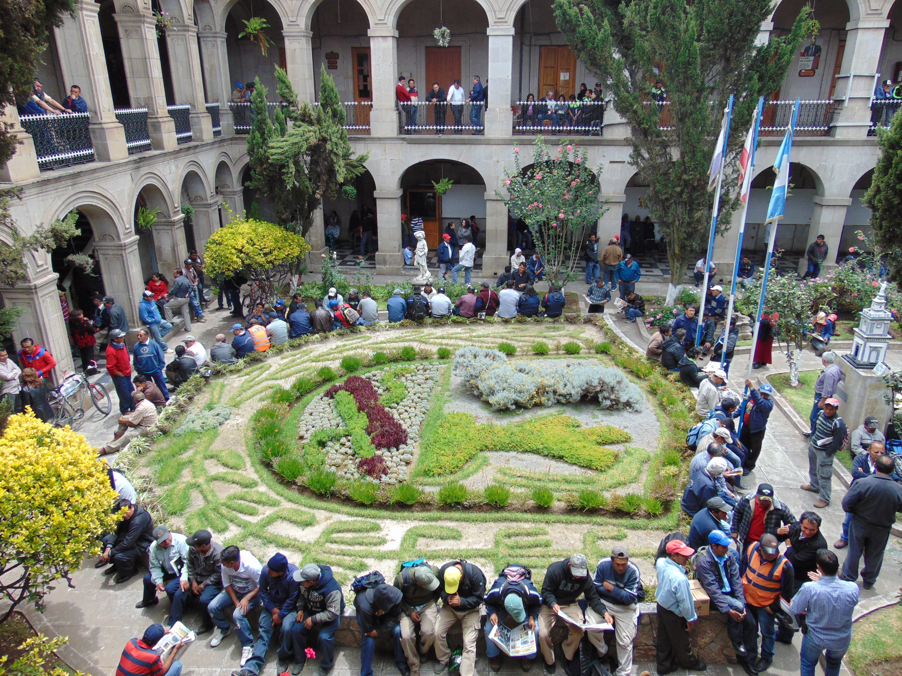 El escudo de la ciudad representado en el Jardín del Palacio Municipal de la Municipalidad de Quetzaltenango, rodeado de Trabajadores sindicalistas, exigiendo sus derechos.